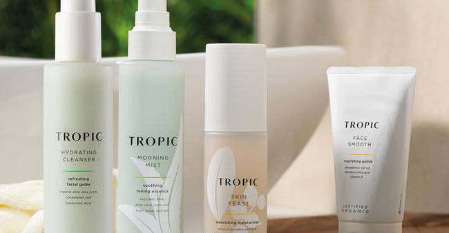 Four Tropic skincare products displayed on a bathroom counter. From left to right: Tropic Hydrating Cleanser in a frosted bottle with pump, Tropic Morning Mist in a similar frosted bottle, Tropic Skin Feast nourishing moisturiser in a sleek bottle, and Tropic Face Smooth nourishing polish in a white squeeze tube.